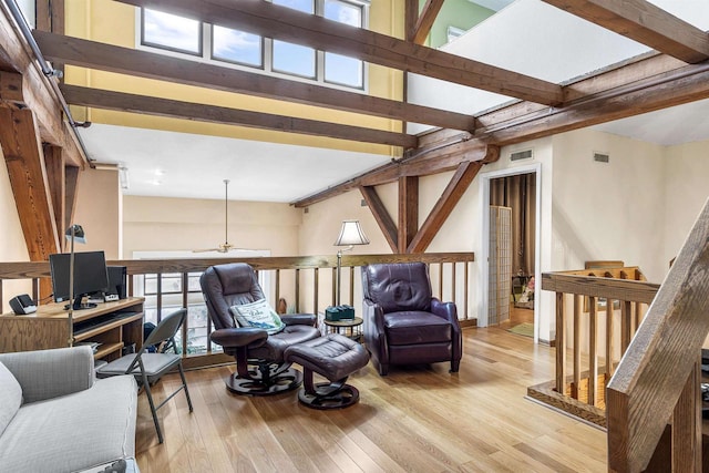 living area featuring beam ceiling, ceiling fan, and light wood-type flooring