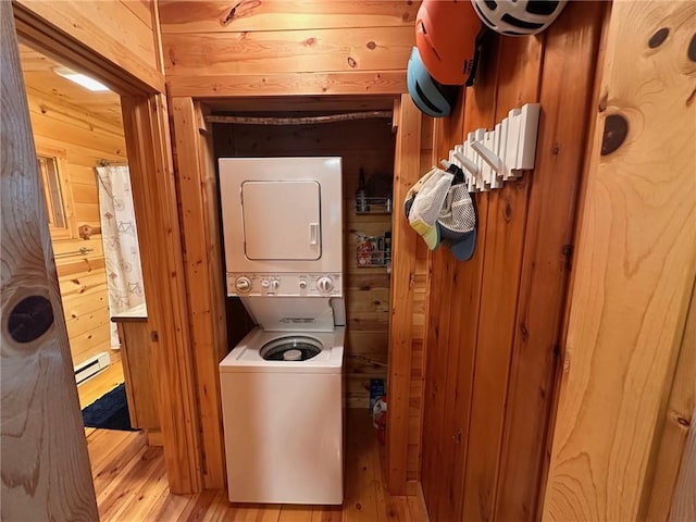 clothes washing area with stacked washer / drying machine, wood walls, light hardwood / wood-style floors, and a baseboard radiator