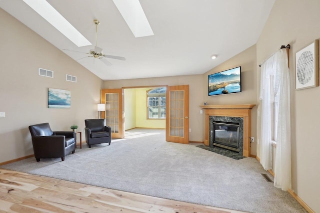 living room with ceiling fan, french doors, a premium fireplace, lofted ceiling with skylight, and light carpet