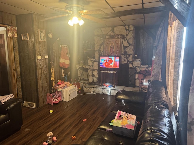 living room with hardwood / wood-style floors, a paneled ceiling, ceiling fan, and wooden walls