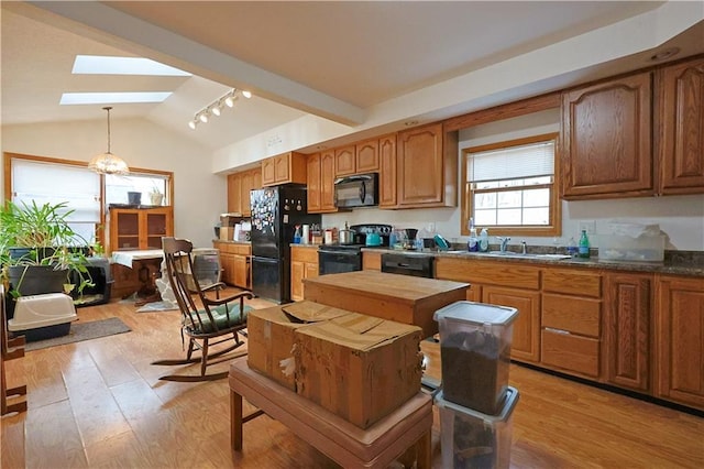 kitchen featuring vaulted ceiling with skylight, black appliances, decorative light fixtures, and light hardwood / wood-style floors