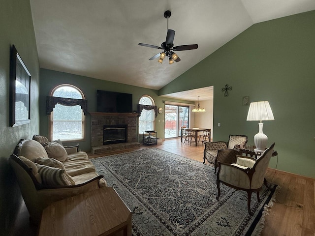 living room featuring hardwood / wood-style floors, ceiling fan with notable chandelier, a fireplace, and vaulted ceiling