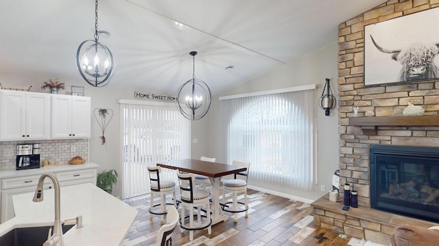 kitchen featuring backsplash, sink, hanging light fixtures, vaulted ceiling, and white cabinetry