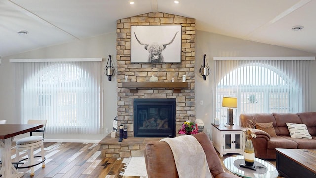 living room with hardwood / wood-style flooring, a stone fireplace, and lofted ceiling