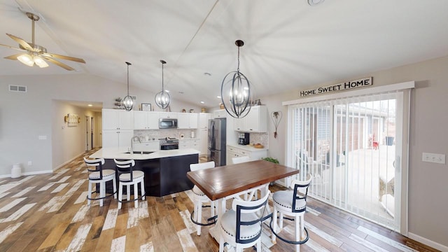 dining space with sink, ceiling fan with notable chandelier, lofted ceiling, and light wood-type flooring