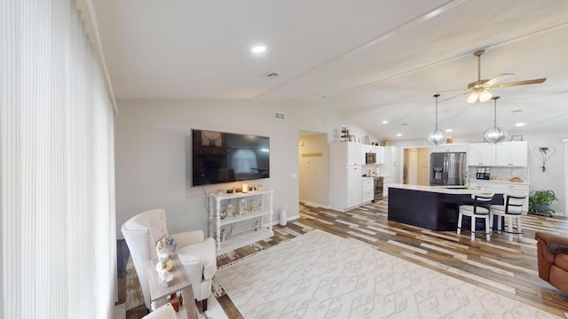 living room featuring ceiling fan, light hardwood / wood-style floors, and vaulted ceiling