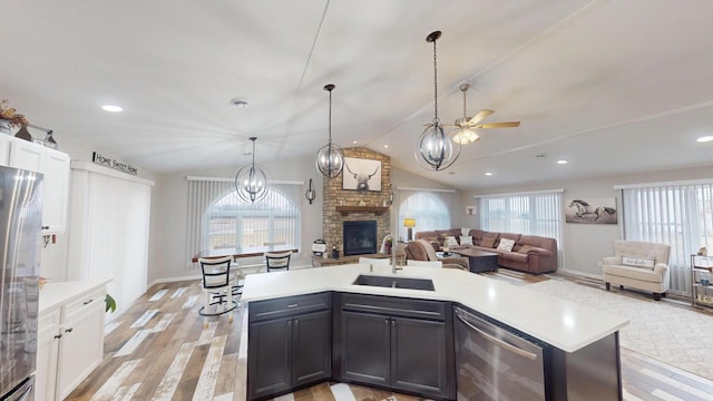 kitchen featuring lofted ceiling, a center island with sink, a stone fireplace, sink, and white cabinetry