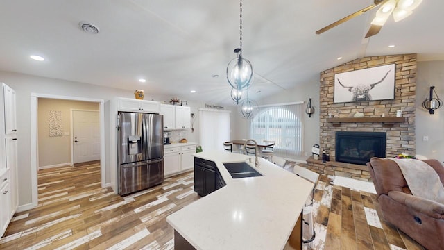 kitchen with white cabinets, a center island with sink, sink, stainless steel fridge, and decorative light fixtures