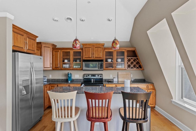 kitchen with stainless steel appliances, dark stone countertops, decorative light fixtures, a kitchen bar, and a kitchen island