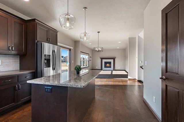 kitchen with pendant lighting, dark hardwood / wood-style floors, light stone countertops, dark brown cabinets, and stainless steel fridge with ice dispenser