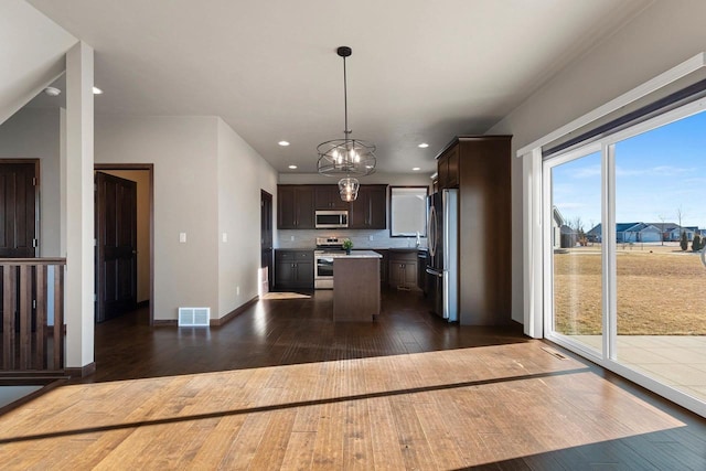 kitchen featuring a center island, dark wood-type flooring, appliances with stainless steel finishes, decorative light fixtures, and dark brown cabinets