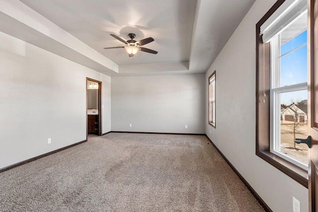 carpeted empty room with a raised ceiling, a wealth of natural light, and ceiling fan