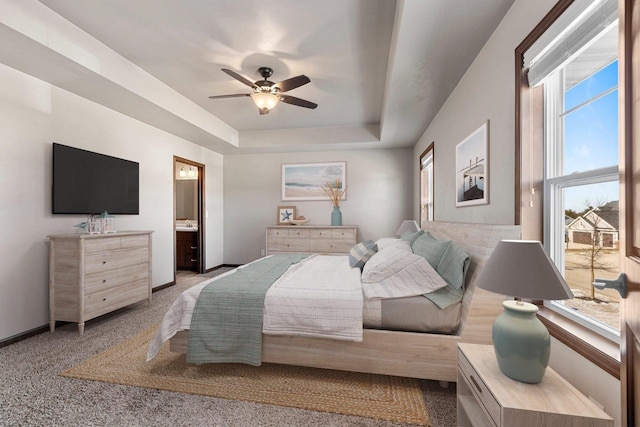 bedroom featuring a raised ceiling, connected bathroom, ceiling fan, and light colored carpet