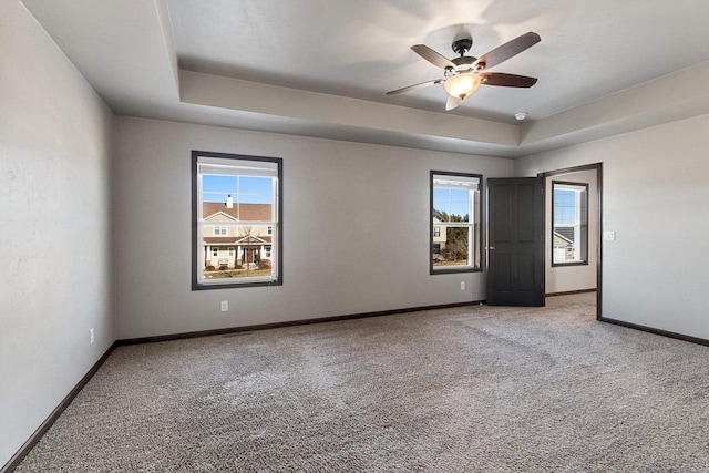 carpeted empty room with a wealth of natural light, a raised ceiling, and ceiling fan