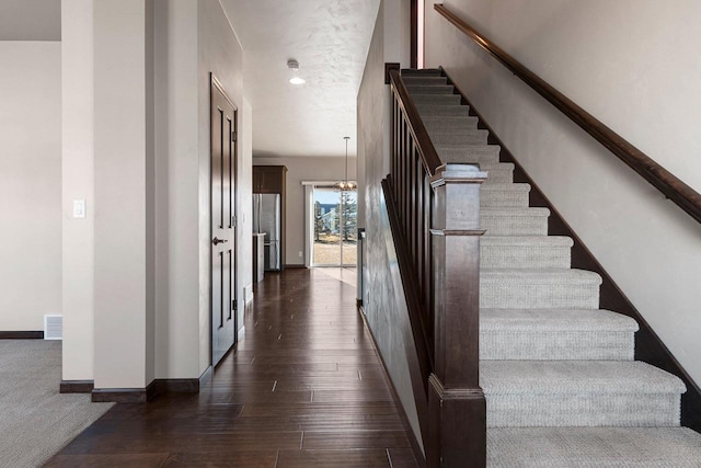 stairway with wood-type flooring and a chandelier