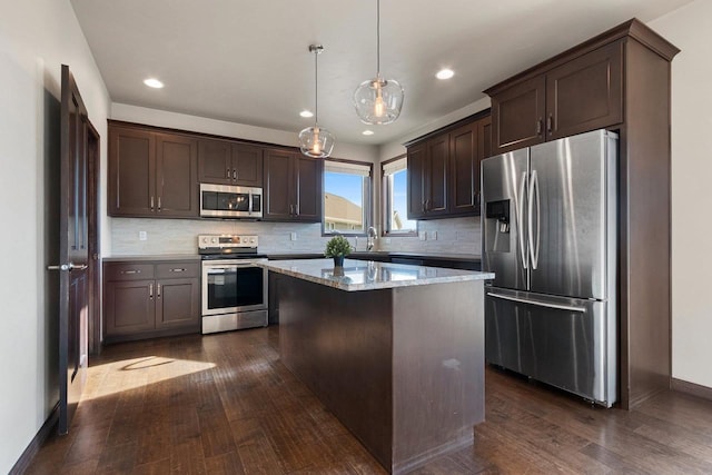 kitchen with light stone countertops, appliances with stainless steel finishes, a center island, dark hardwood / wood-style floors, and hanging light fixtures