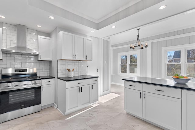 kitchen with a wealth of natural light, stainless steel range, wall chimney range hood, an inviting chandelier, and white cabinets