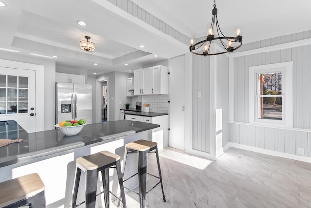 kitchen with a kitchen breakfast bar, white cabinets, hanging light fixtures, and stainless steel refrigerator with ice dispenser