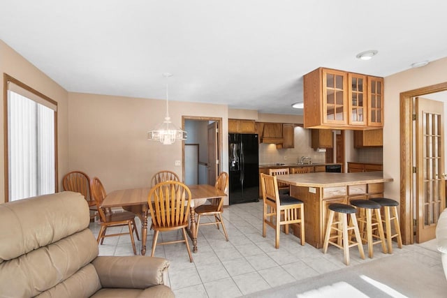 kitchen featuring a kitchen bar, black fridge, tasteful backsplash, hanging light fixtures, and light tile patterned floors