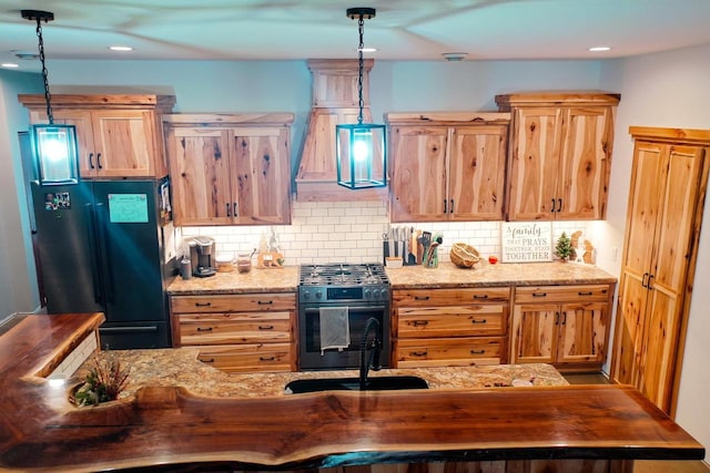 kitchen with black refrigerator, hanging light fixtures, light stone countertops, and stainless steel gas range