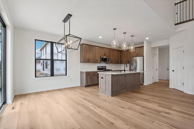 kitchen featuring hanging light fixtures, decorative backsplash, light wood-type flooring, an island with sink, and stainless steel appliances