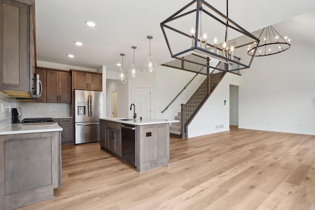 kitchen with sink, light hardwood / wood-style flooring, an island with sink, decorative light fixtures, and stainless steel appliances