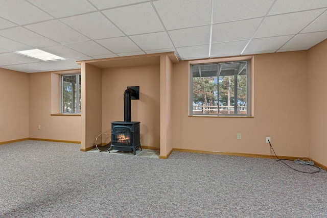 unfurnished living room with light carpet, a drop ceiling, a wood stove, and a wealth of natural light