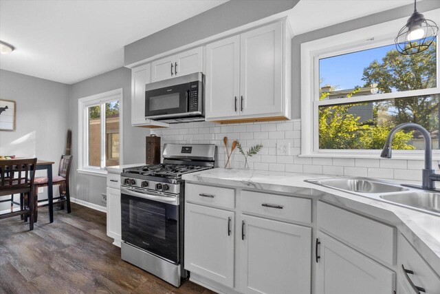 kitchen featuring stainless steel gas range, sink, dark hardwood / wood-style floors, white cabinetry, and hanging light fixtures