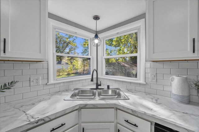 kitchen featuring pendant lighting, sink, decorative backsplash, light stone countertops, and white cabinetry