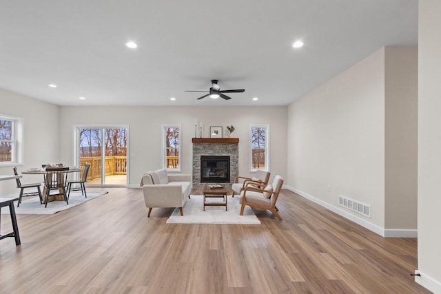 living room with light hardwood / wood-style floors, a stone fireplace, and ceiling fan