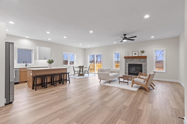 living room with a stone fireplace, sink, ceiling fan, plenty of natural light, and light hardwood / wood-style floors