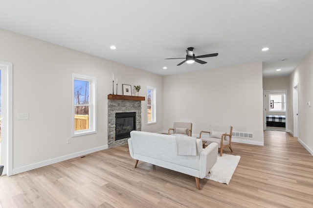 living room with ceiling fan, a stone fireplace, and light wood-type flooring