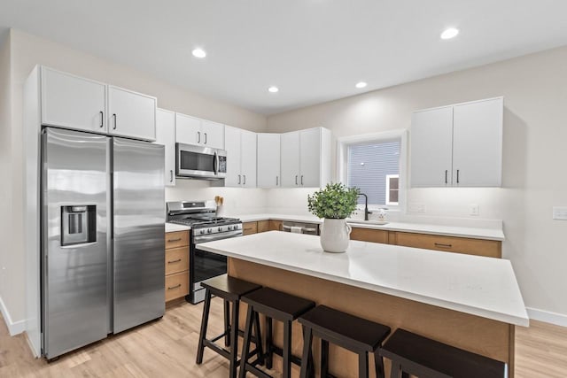 kitchen with white cabinets, a center island, light wood-type flooring, and appliances with stainless steel finishes