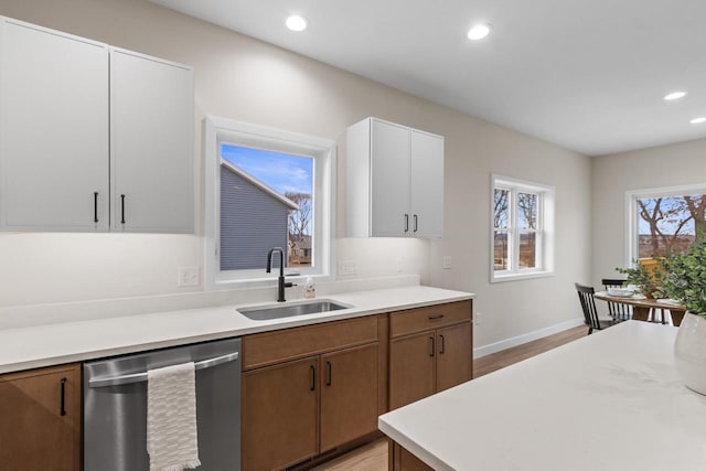 kitchen with stainless steel dishwasher, white cabinets, light wood-type flooring, and sink