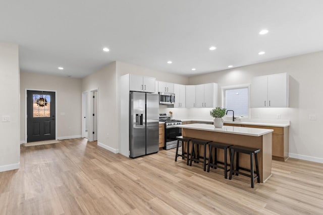 kitchen featuring appliances with stainless steel finishes, a breakfast bar, sink, white cabinets, and a kitchen island