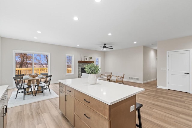 kitchen featuring a kitchen bar, ceiling fan, a fireplace, a center island, and light hardwood / wood-style floors