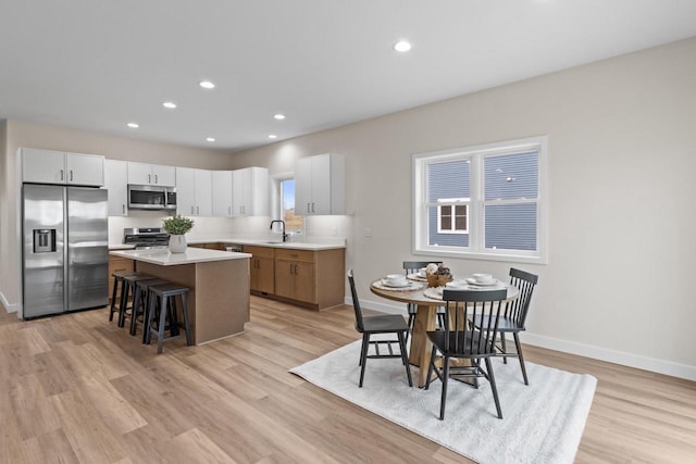 kitchen with appliances with stainless steel finishes, light wood-type flooring, a kitchen breakfast bar, white cabinets, and a center island