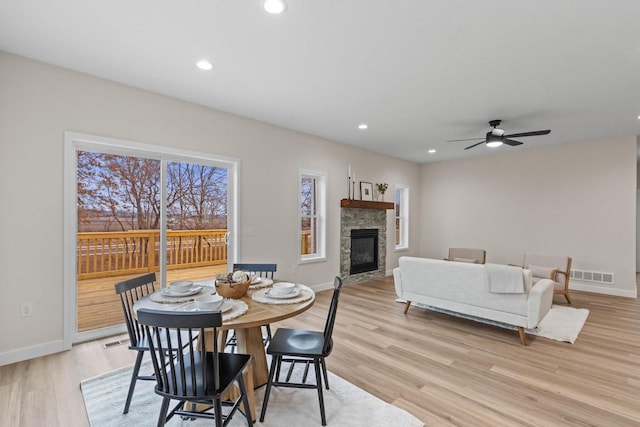 dining area featuring a stone fireplace, ceiling fan, and light hardwood / wood-style flooring