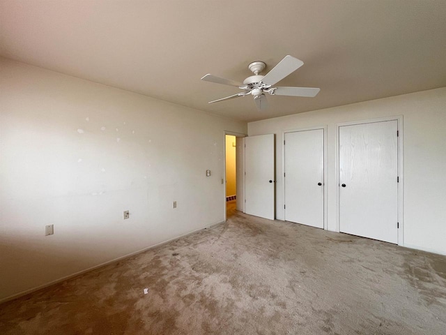 unfurnished bedroom with carpet, two closets, and ceiling fan