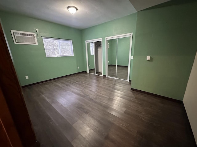 unfurnished bedroom with two closets, a wall mounted AC, and dark wood-type flooring