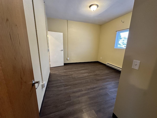 unfurnished room with dark wood-type flooring and a baseboard heating unit