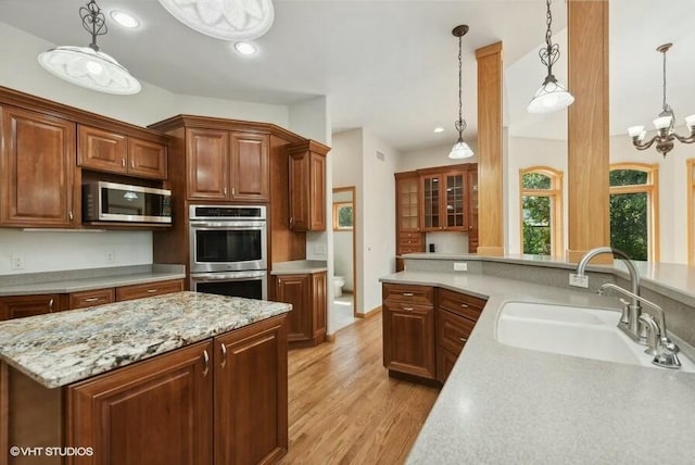 kitchen featuring sink, a chandelier, light wood-type flooring, appliances with stainless steel finishes, and pendant lighting