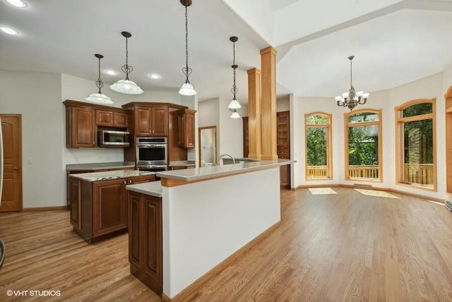 kitchen with hanging light fixtures, light wood-type flooring, an island with sink, a notable chandelier, and stainless steel appliances