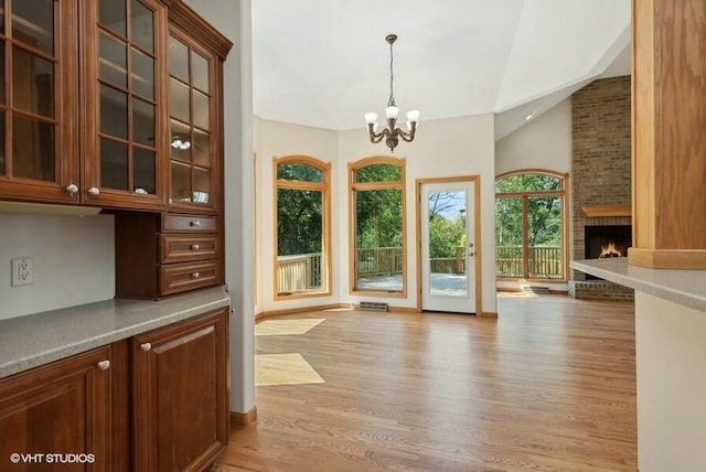 entryway with vaulted ceiling, a large fireplace, a chandelier, and light hardwood / wood-style floors