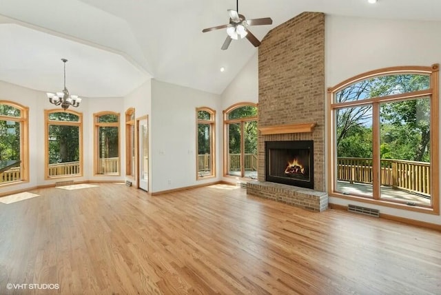 unfurnished living room with a brick fireplace, ceiling fan with notable chandelier, high vaulted ceiling, and light hardwood / wood-style floors