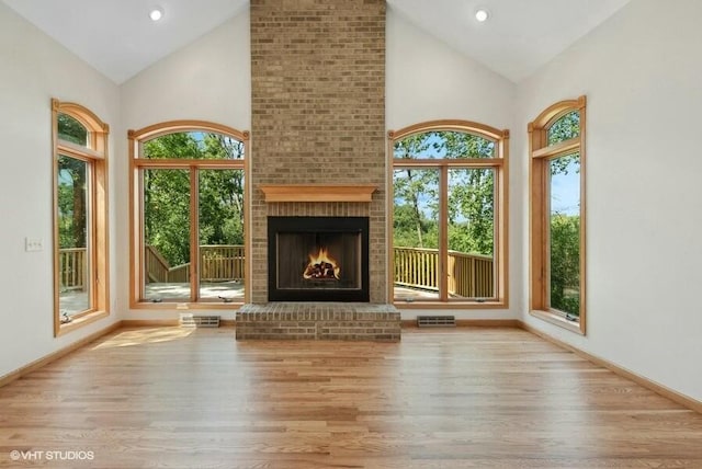 unfurnished living room with high vaulted ceiling, a fireplace, and light hardwood / wood-style floors