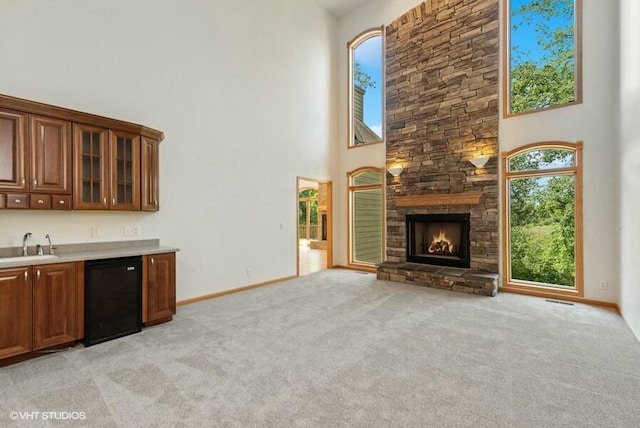 unfurnished living room featuring light carpet, sink, a stone fireplace, and a high ceiling