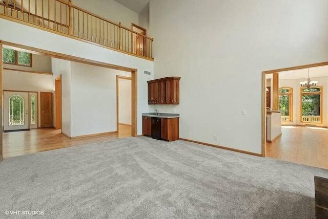 unfurnished living room featuring an inviting chandelier, light colored carpet, and a high ceiling