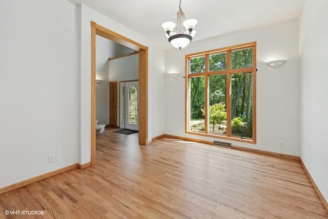 empty room with a healthy amount of sunlight, a chandelier, and light hardwood / wood-style flooring