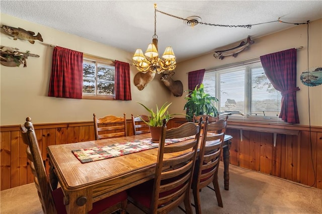 carpeted dining area with a chandelier, a textured ceiling, and wood walls